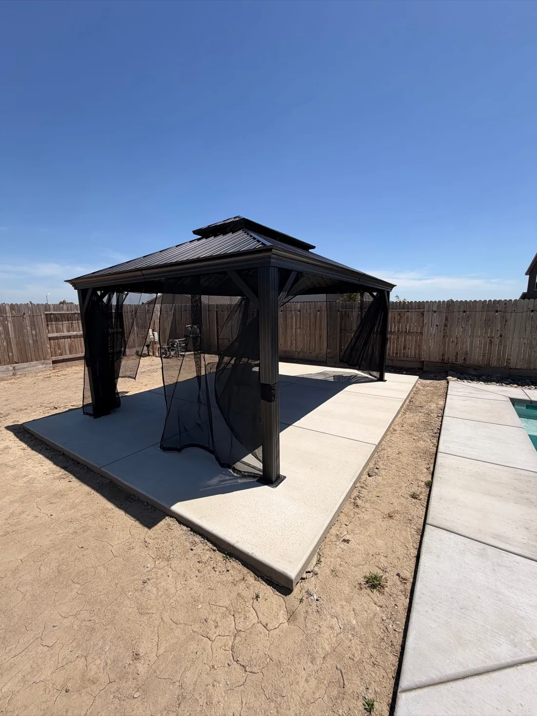 Black metal gazebo with retractable curtains installed on concrete patio — Zomg The Handyman