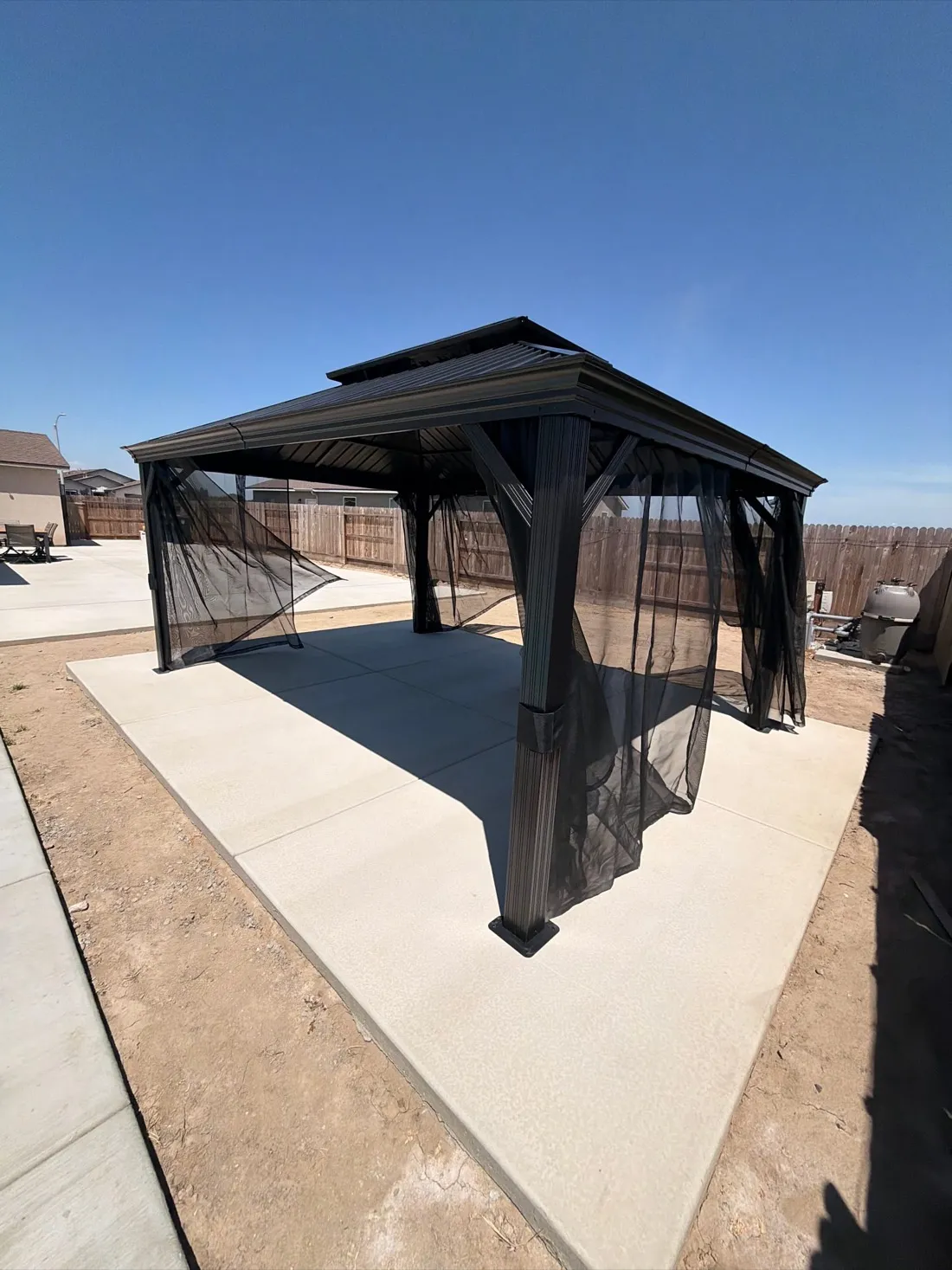 Black metal gazebo with mesh curtains installed on concrete patio foundation. — Zomg The Handyman