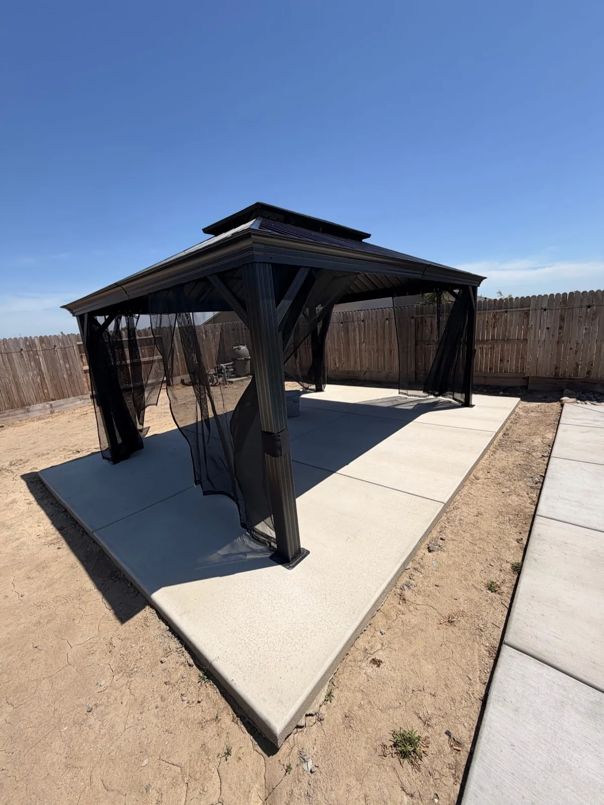 Black metal gazebo anchored to a concrete patio foundation