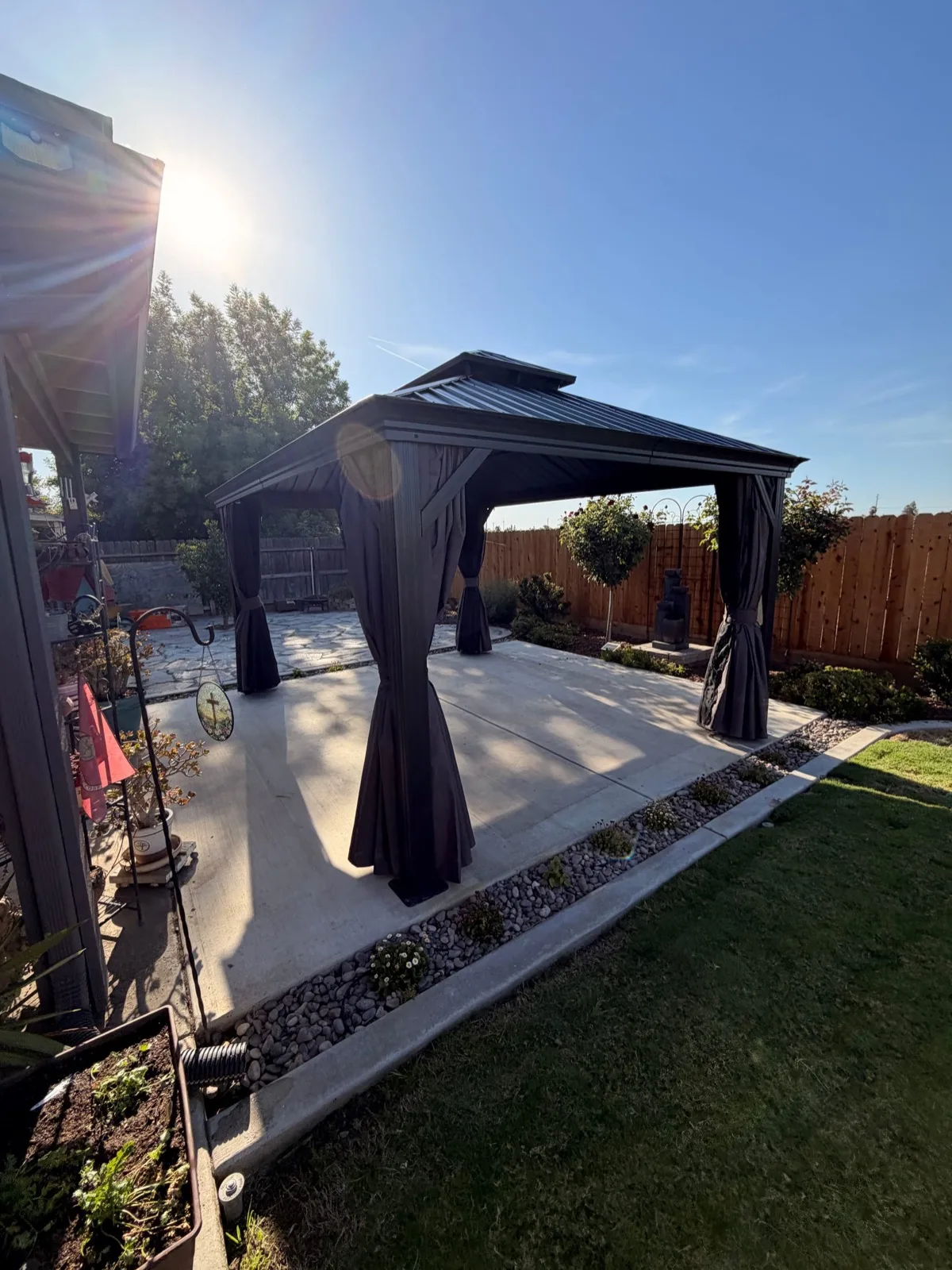 Black metal gazebo with retractable curtains assembled on a concrete patio by Zomg The Handyman