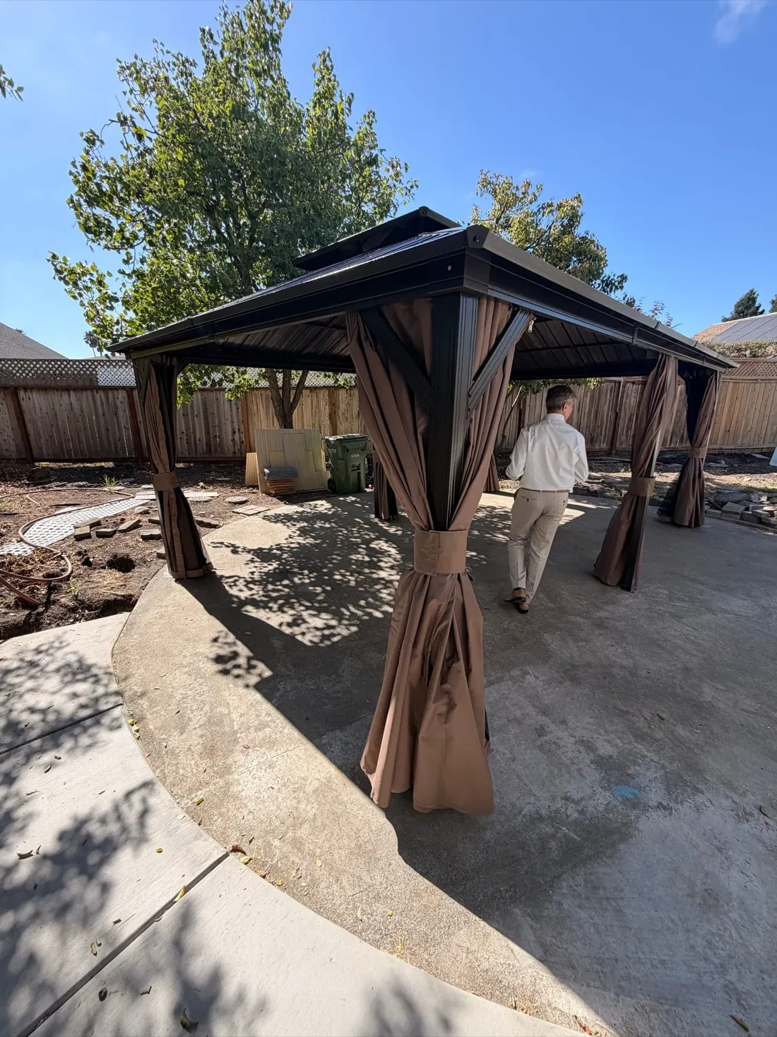 Brown hardtop gazebo with privacy curtains assembled on a circular concrete pad — Zomg The Handyman